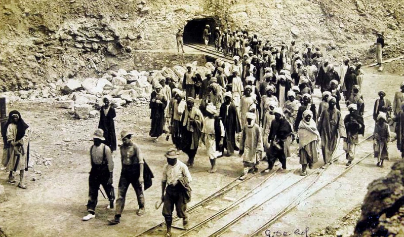 Workers leaving an El Quseir mine c 1930. A possible overseer, right, wearing a colonial pith helmet, watches. 
Public domain via Wikimedia